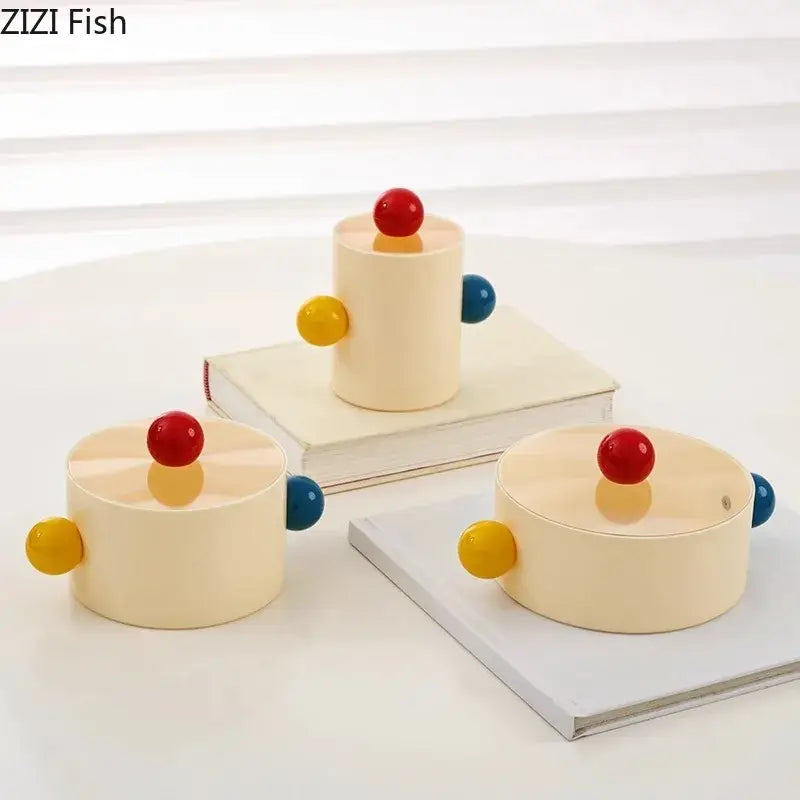 Cream-colored cylindrical storage jar with colorful dot decorative handles and red lids by zizi fish for bedroom organization