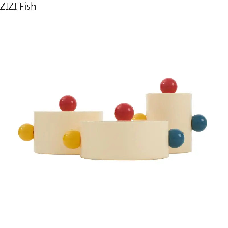 Cream-colored cylindrical ceramic storage jar with colorful dot decorative spheres in red yellow and blue for bedroom organization