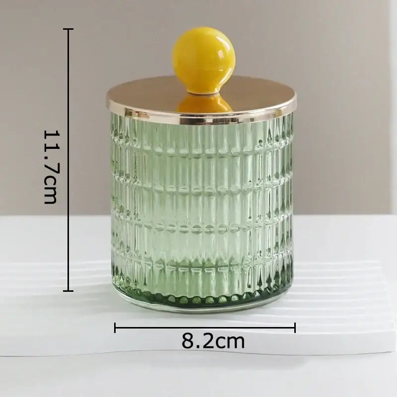 A translucent green glass tea canister with vertical ridges and a gold-toned storage jar lid with yellow knob