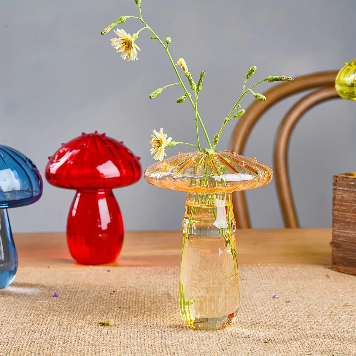Transparent amber glass mushroom-shaped vase with textured cap holding delicate yellow flowers for living room decor