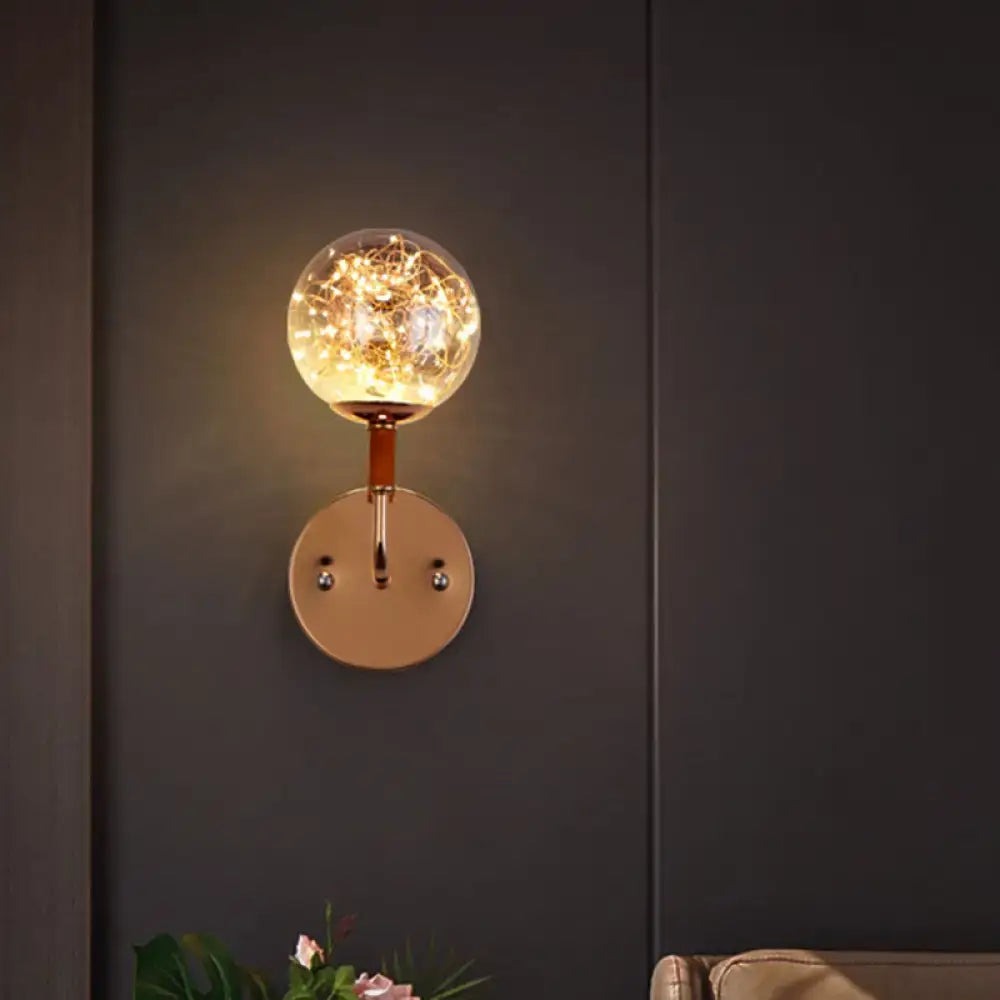 Contemporary amber glass direct wired electric bedroom wall sconce with warm-toned spherical glass globe and rose gold base