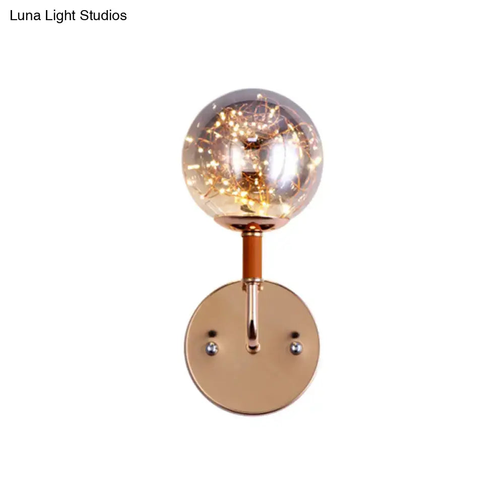 Contemporary rose gold direct wired electric bedroom wall sconce with clear amber glass globe housing warm fairy lights
