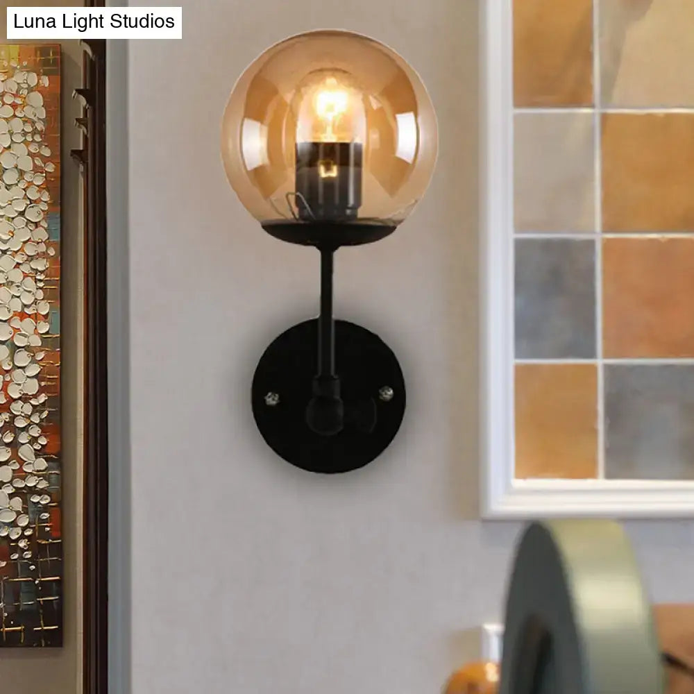 Contemporary black metal wall light with warm amber globe glass shade featuring an exposed bulb for bedroom use