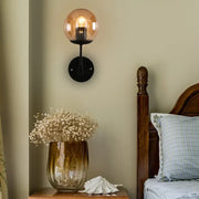 Contemporary wall light featuring warm amber globe glass shade with black metal base for bedroom use