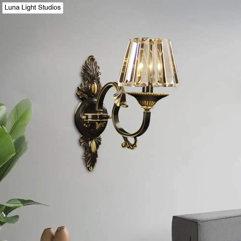 Antique brass wall light featuring a tiered crystal prism shade in a contemporary wall mounted bedroom sconce design