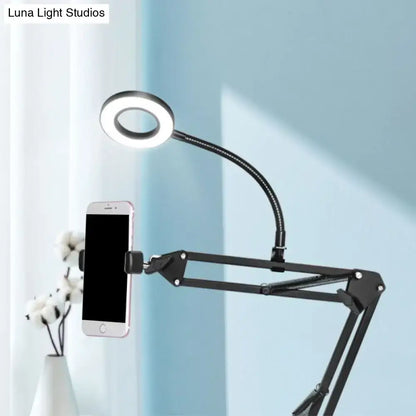 Contemporary black metal ring vanity desk lamp with adjustable arm and flexible gooseneck holding a smartphone