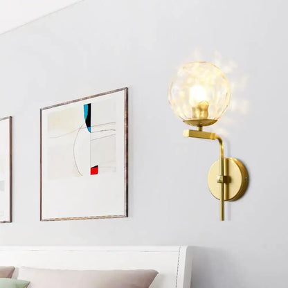 Contemporary gold-toned wall mount lighting with a faceted translucent glass globe for bedroom use
