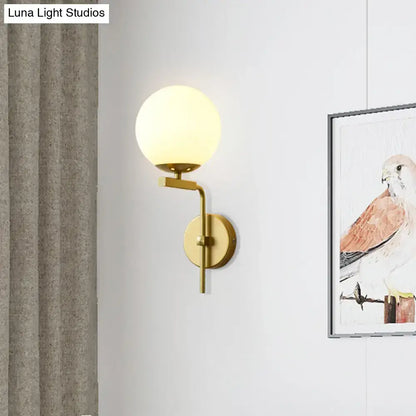 Gold-toned wall mount lighting with frosted glass globe in contemporary black sphere design for bedroom use