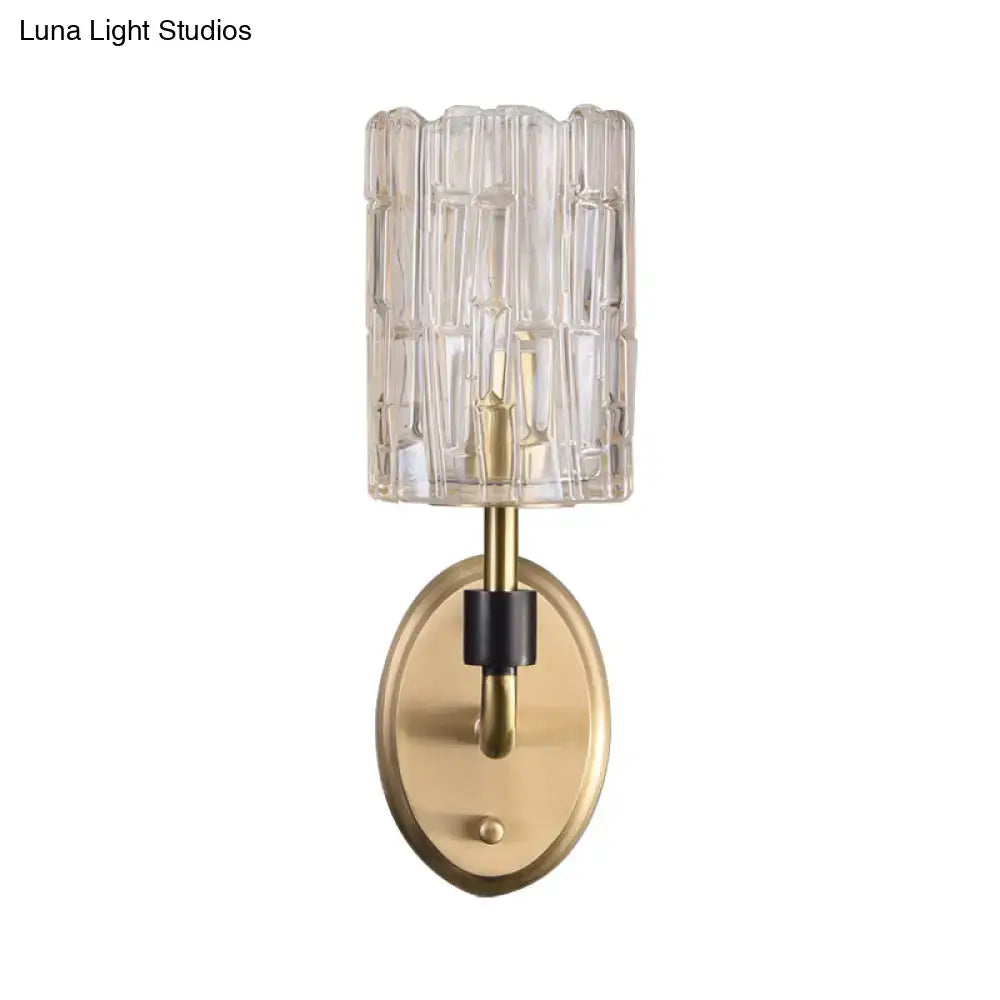 Contemporary brass bedside wall sconce with clear crystal shade featuring a cylindrical glass shade with vertical ridges
