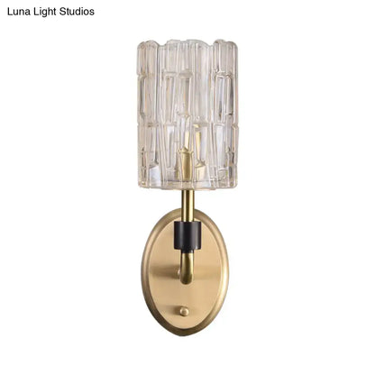 Contemporary brass bedside wall sconce with clear crystal shade featuring a cylindrical glass shade with vertical ridges