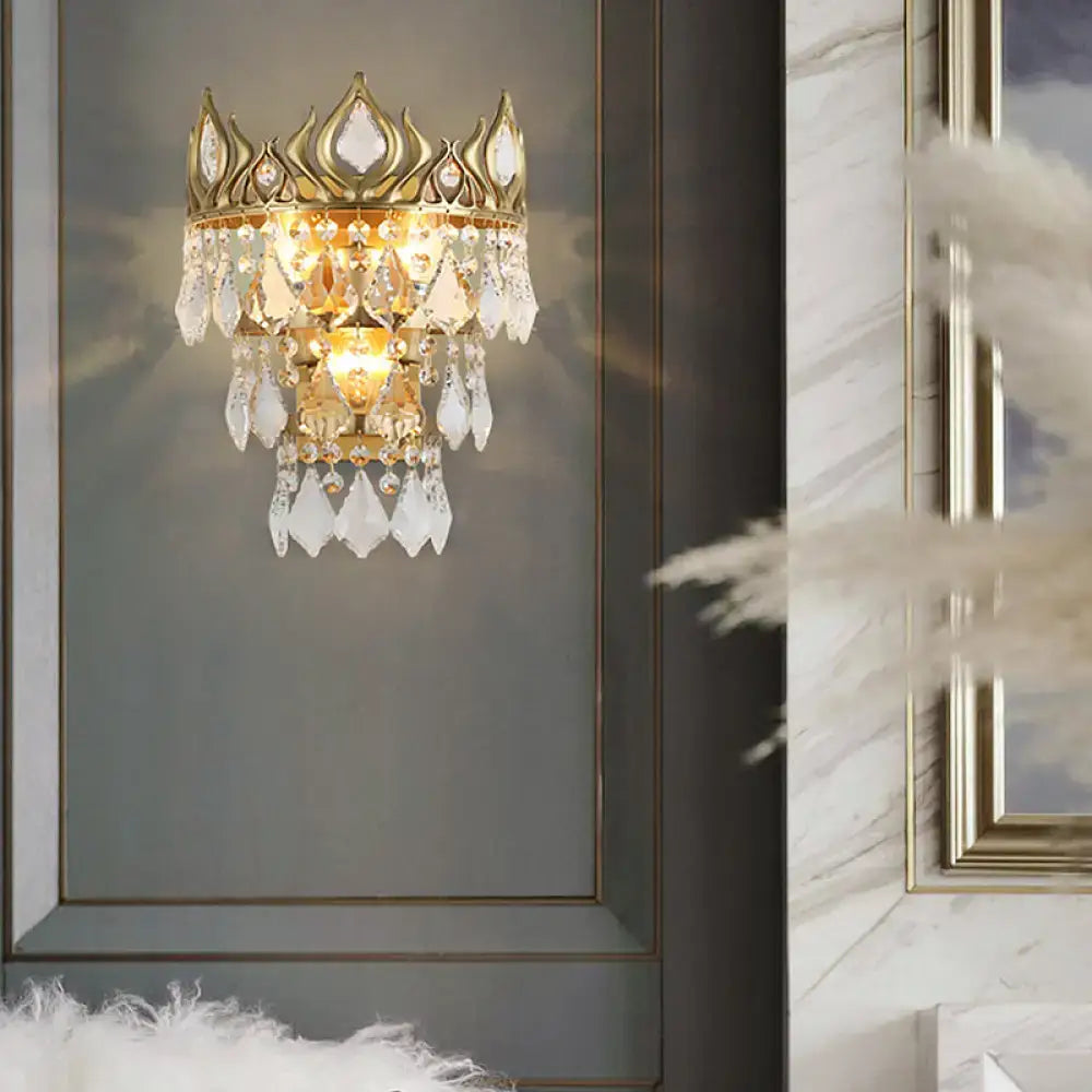 Contemporary brass crown sconce light fixture in gold tone with cascading clear crystal droplets for bedroom lighting