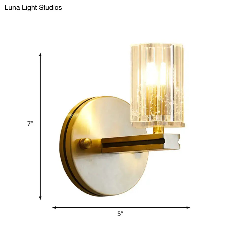 Contemporary brass crystal cylinder sconce light with a gold-toned metal arm and prismatic crystal cylinder shade for bedroom wall mount