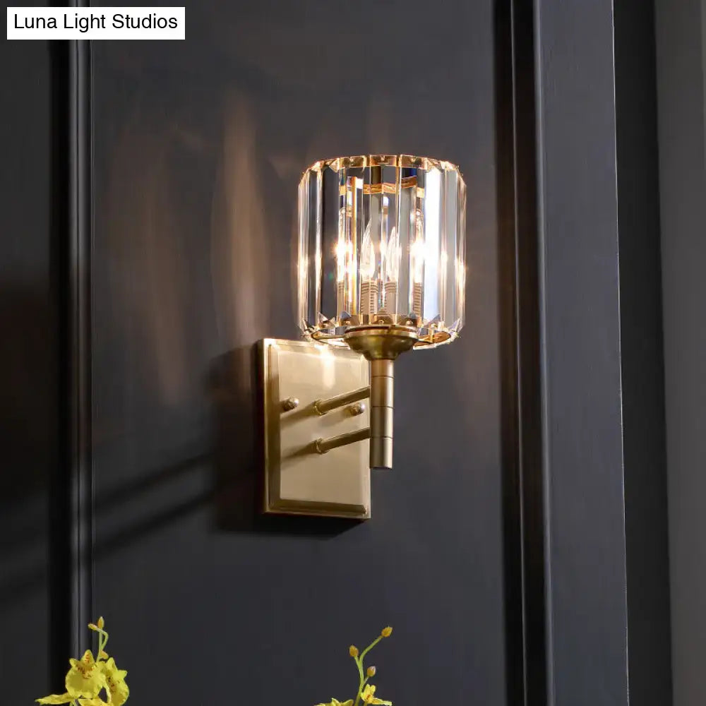 Contemporary brass wall sconce with cylindrical crystal shade for bedroom lighting in polished brass finish