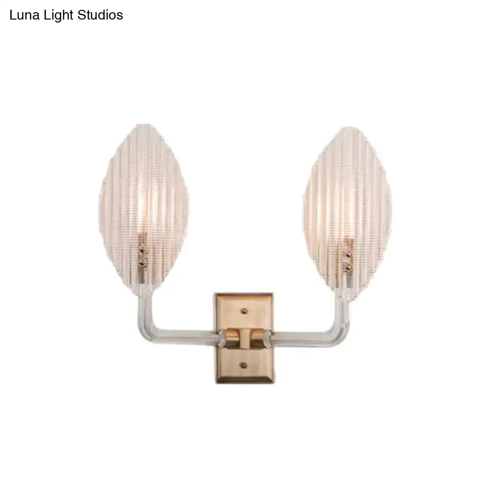 A contemporary brass leaf wall light fixture with two glass shades and brushed brass arm for living room use
