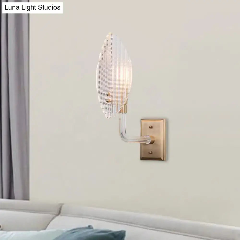 Contemporary brass leaf wall light fixture with clear ribbed glass shade and brass-finished metal base for living room