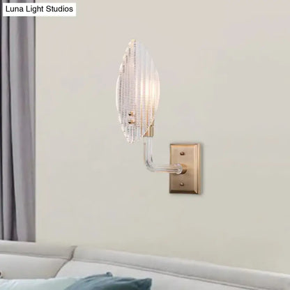 Contemporary brass leaf wall light fixture with clear ribbed glass shade and brass-finished metal base for living room