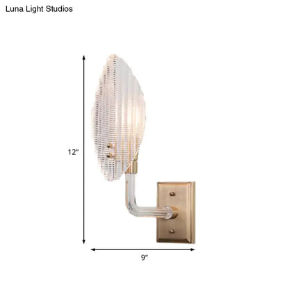 A contemporary brass leaf wall light fixture with a translucent ribbed glass shade for living room use