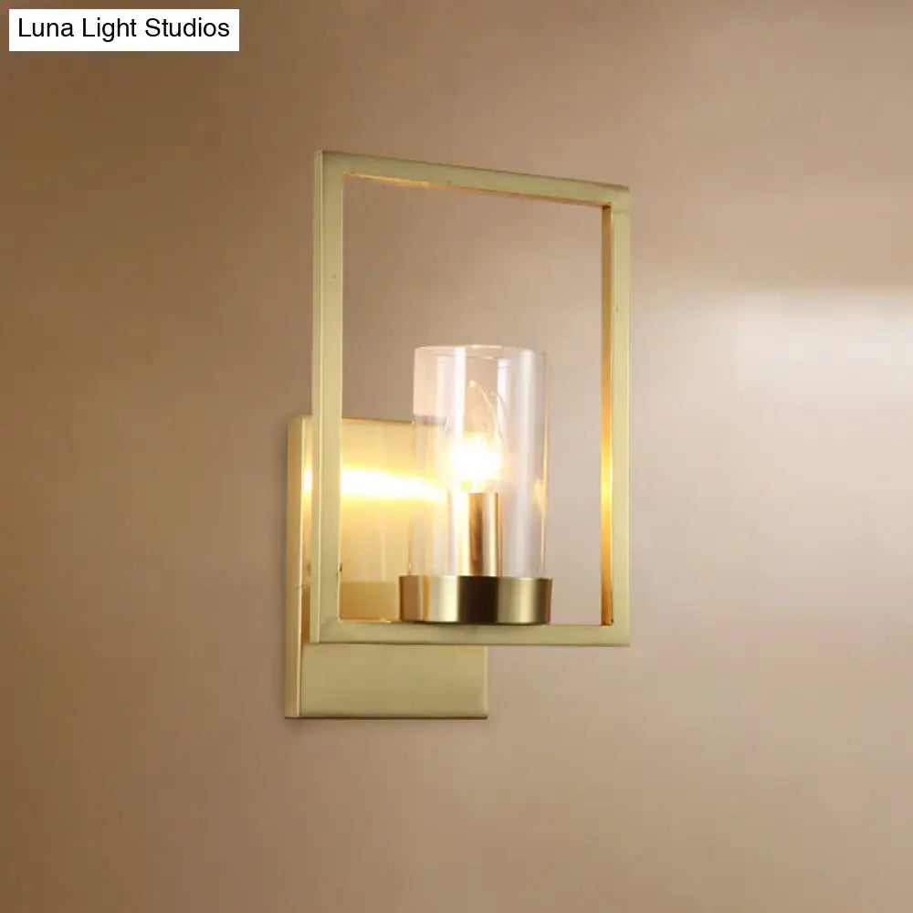 Contemporary brass wall light with gold-toned rectangular frame and clear glass cylinder light fixture for bedroom