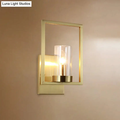 Contemporary brass wall light with gold-toned rectangular frame and clear glass cylinder light fixture for bedroom