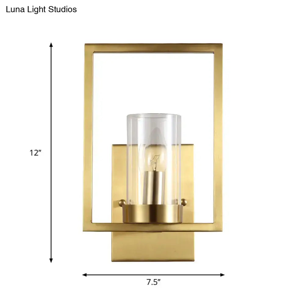 Contemporary brass wall light with gold finish and clear glass cylinder housing an exposed bulb for bedroom use