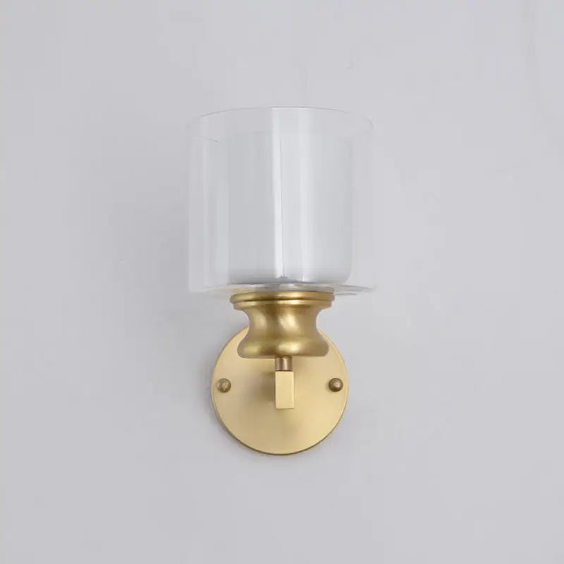 Contemporary brass wall mounted light fixture with gold-toned finish and clear cylindrical glass shade for living room