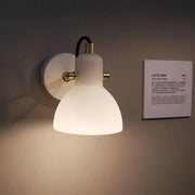 Contemporary wall lamp with white glass domed shade, brass accents, black cord, and adjustable arm for bedroom use