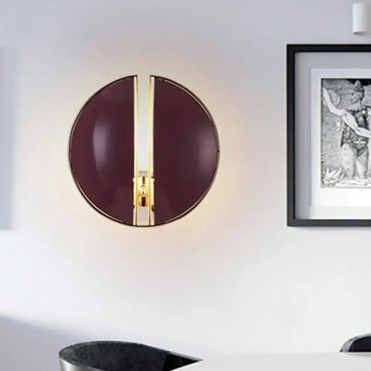 A sleek circular wall lamp with glossy burgundy finish and gold-toned vertical accent for contemporary bedrooms