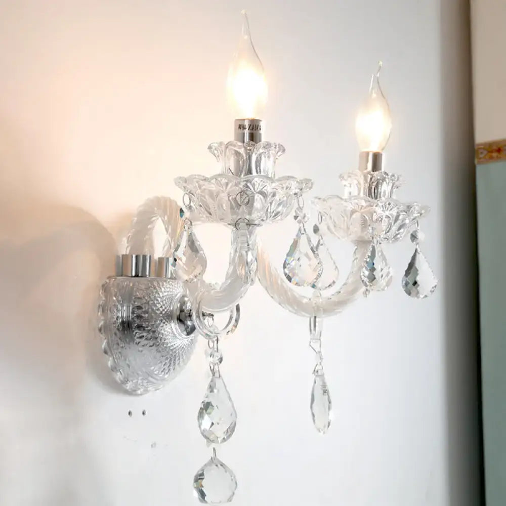 Contemporary clear faceted crystals wall sconce with two lit candle-shaped bulbs and dangling teardrop crystals