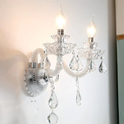 Contemporary clear faceted crystals wall sconce with two lit candle-shaped bulbs and dangling teardrop crystals