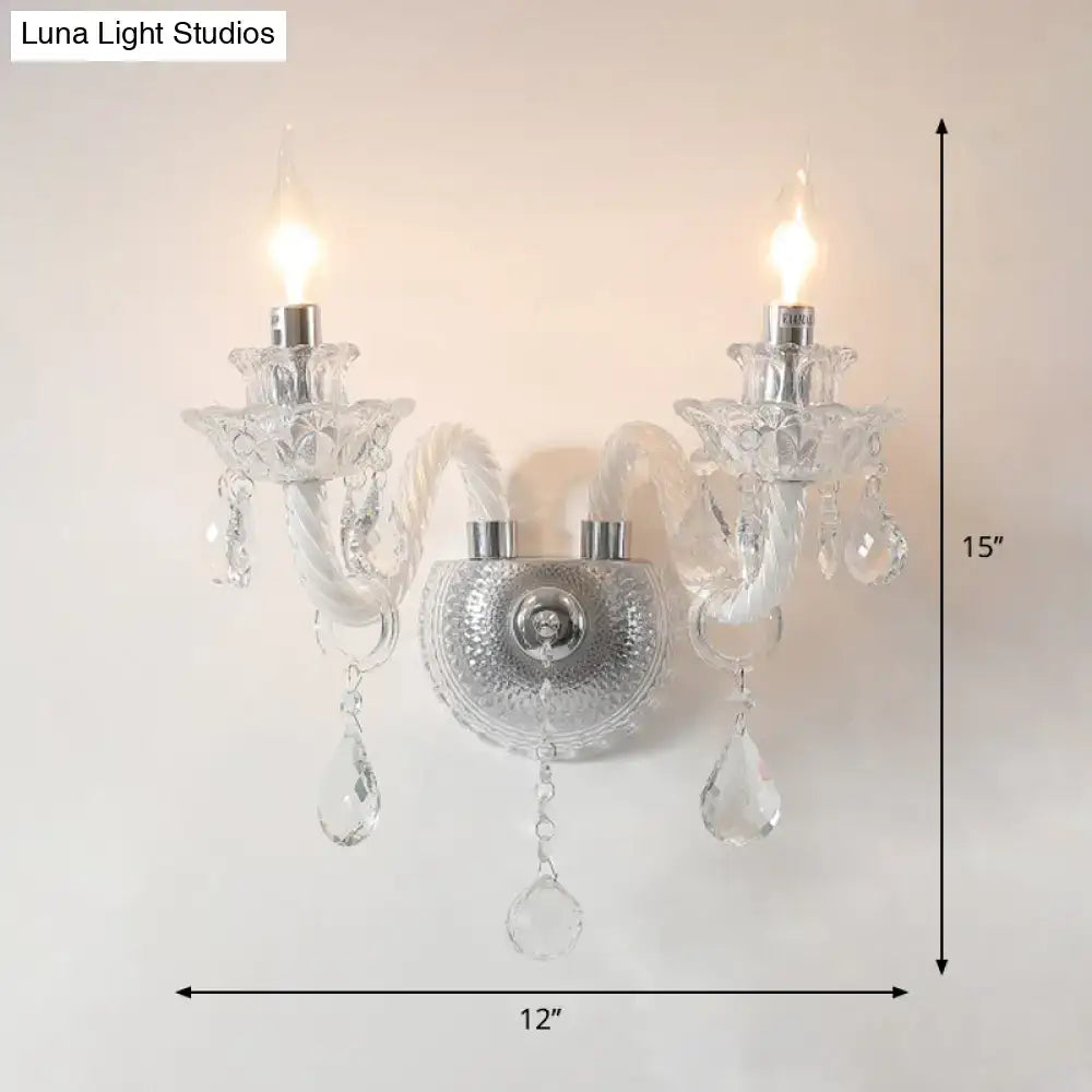 Contemporary crystal chandelier-style wall sconce with clear faceted crystals and two lit candle-like bulbs for living room lighting
