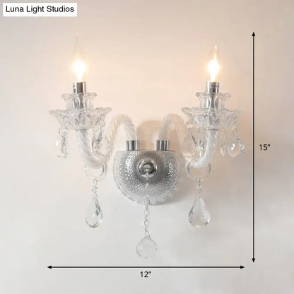 Contemporary crystal chandelier-style wall sconce with clear faceted crystals and two lit candle-like bulbs for living room lighting