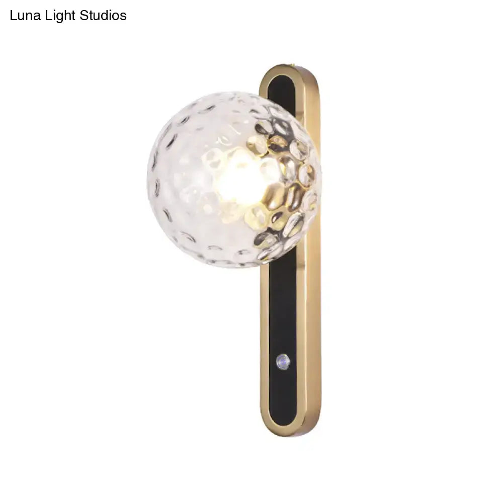 A contemporary clear glass wall lamp with textured globe and gold metal bracket showcasing fixture width
