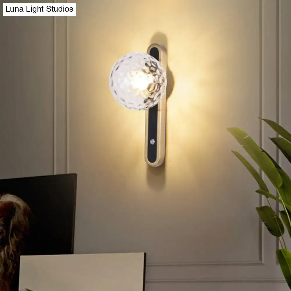 Contemporary clear glass wall lamp with faceted globe and metallic base showcasing fixture width for living room use