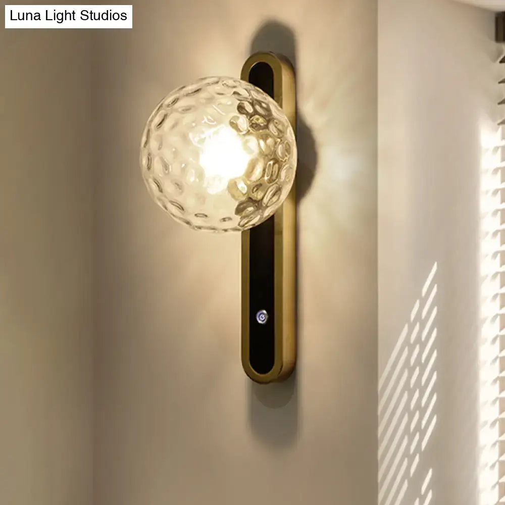 Gold finished contemporary wall lamp with textured clear glass globe and fixture width ideal for living room sconce