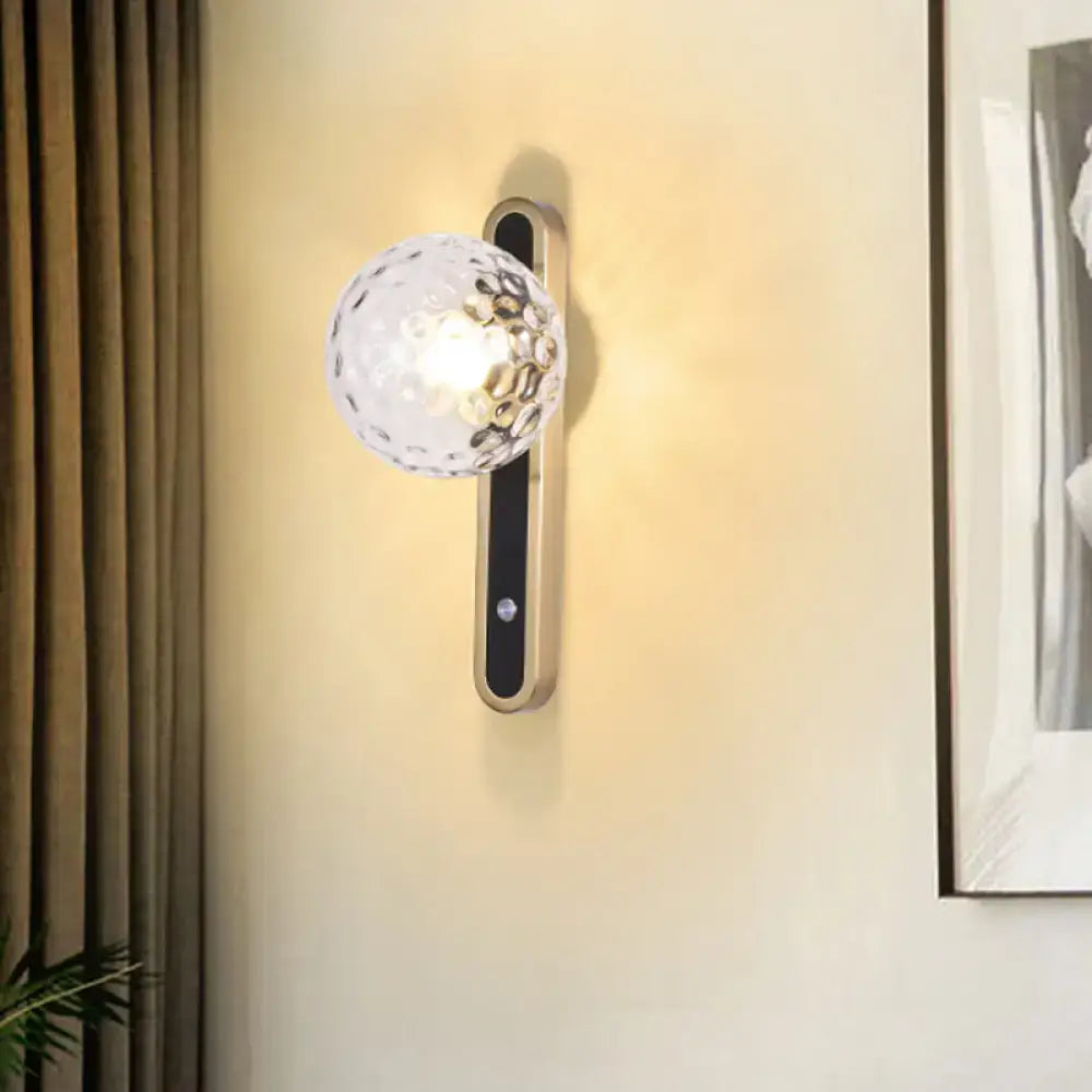 Contemporary clear glass wall lamp with textured globe and black accent panel showcasing fixture width on sconce