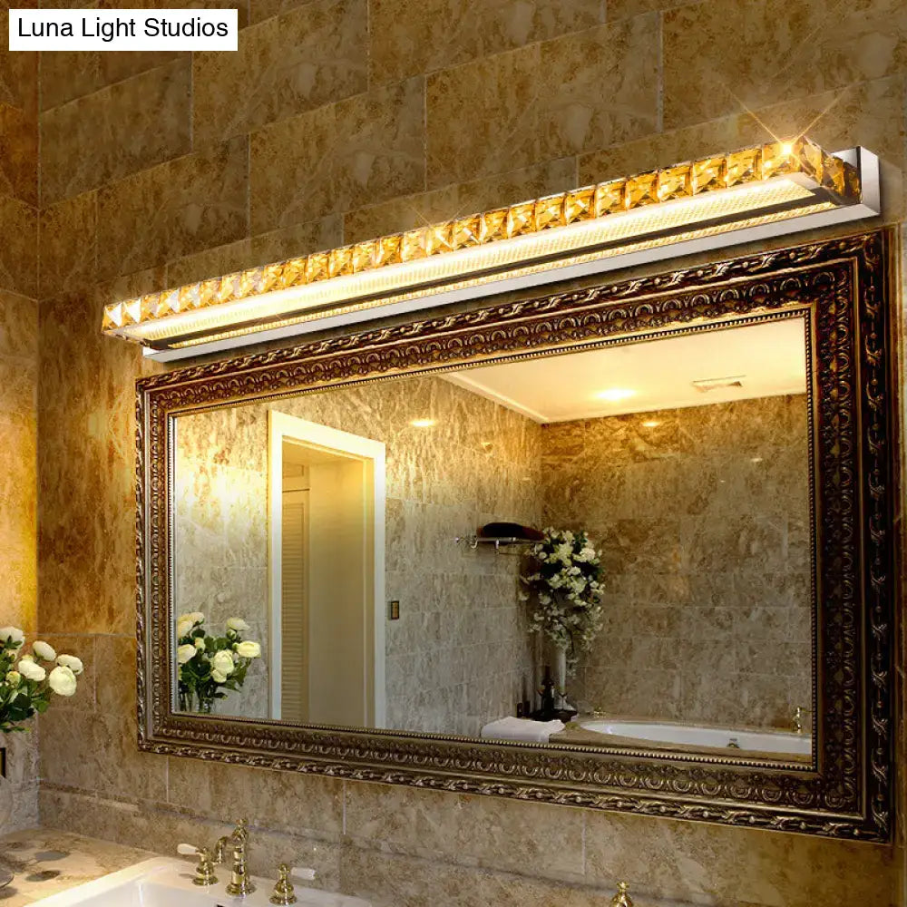 Contemporary crystal gold wall sconce with warm white led light mounted above an ornate bathroom mirror