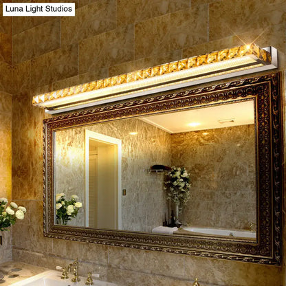 Contemporary crystal gold wall sconce with warm white led light mounted above an ornate bathroom mirror