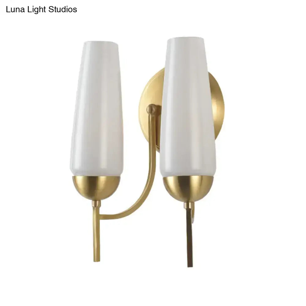 Contemporary gold-toned wall sconce with two frosted white cylindrical shades for bedroom lighting