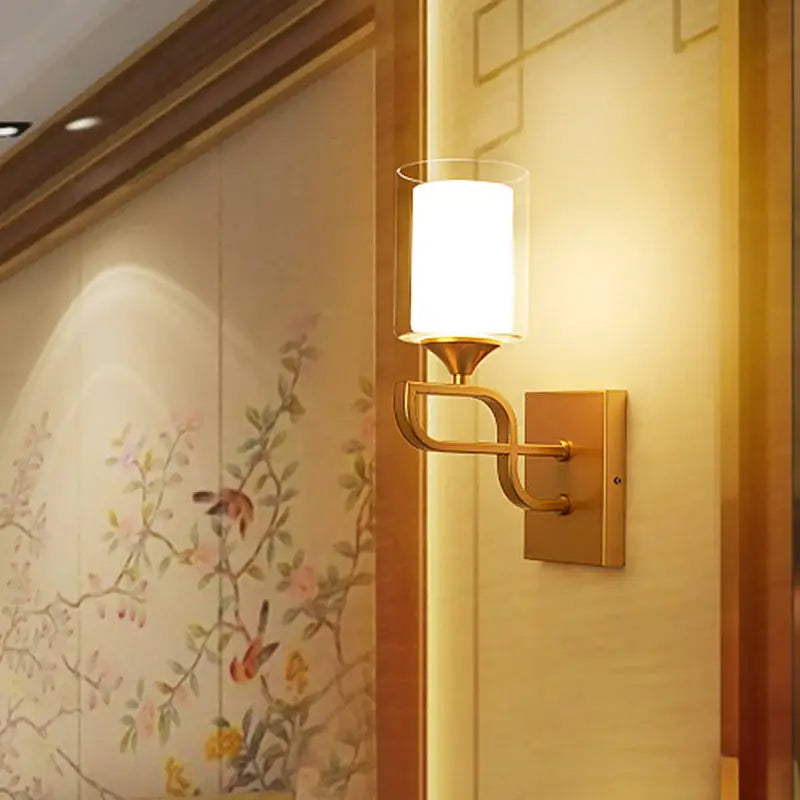 Contemporary gold armed sconce light with cylindrical frosted glass shade and elegant curved metal arm for bedroom use
