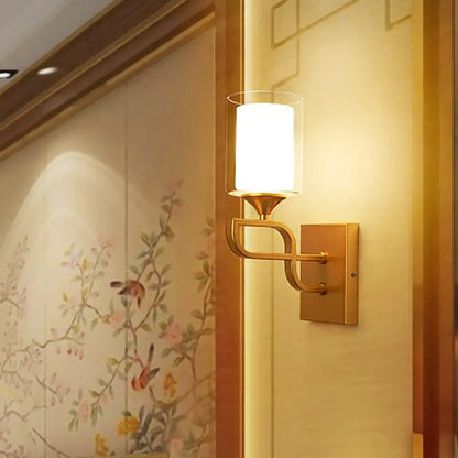 Contemporary gold armed sconce light with cylindrical frosted glass shade and elegant curved metal arm for bedroom use