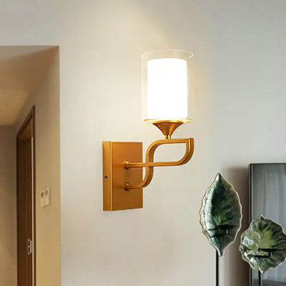 Contemporary gold armed sconce light with a curved modern design and cylindrical frosted opal glass shade