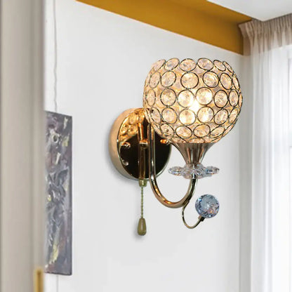 Contemporary gold-toned living room wall sconce with beveled glass globe and dangling faceted glass orb