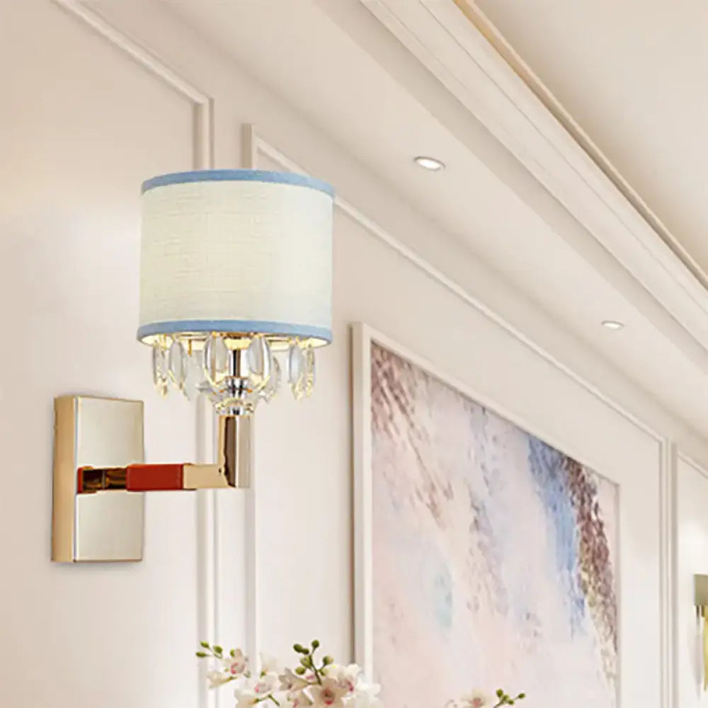 Contemporary wall light with a crystal deco design, gold polished arm, and cream drum fabric shade with blue trim