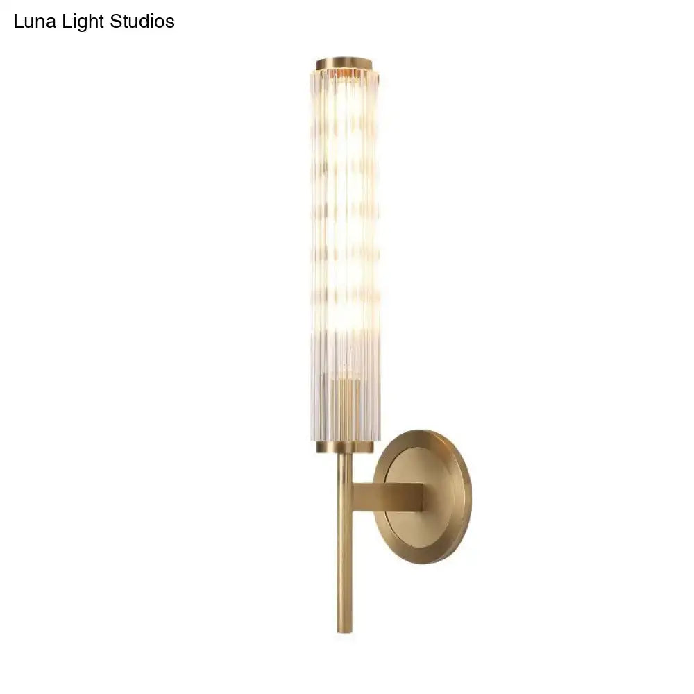 Contemporary gold brass wall light fixture with cylindrical ridged glass shade and illuminated light bulb for bedroom