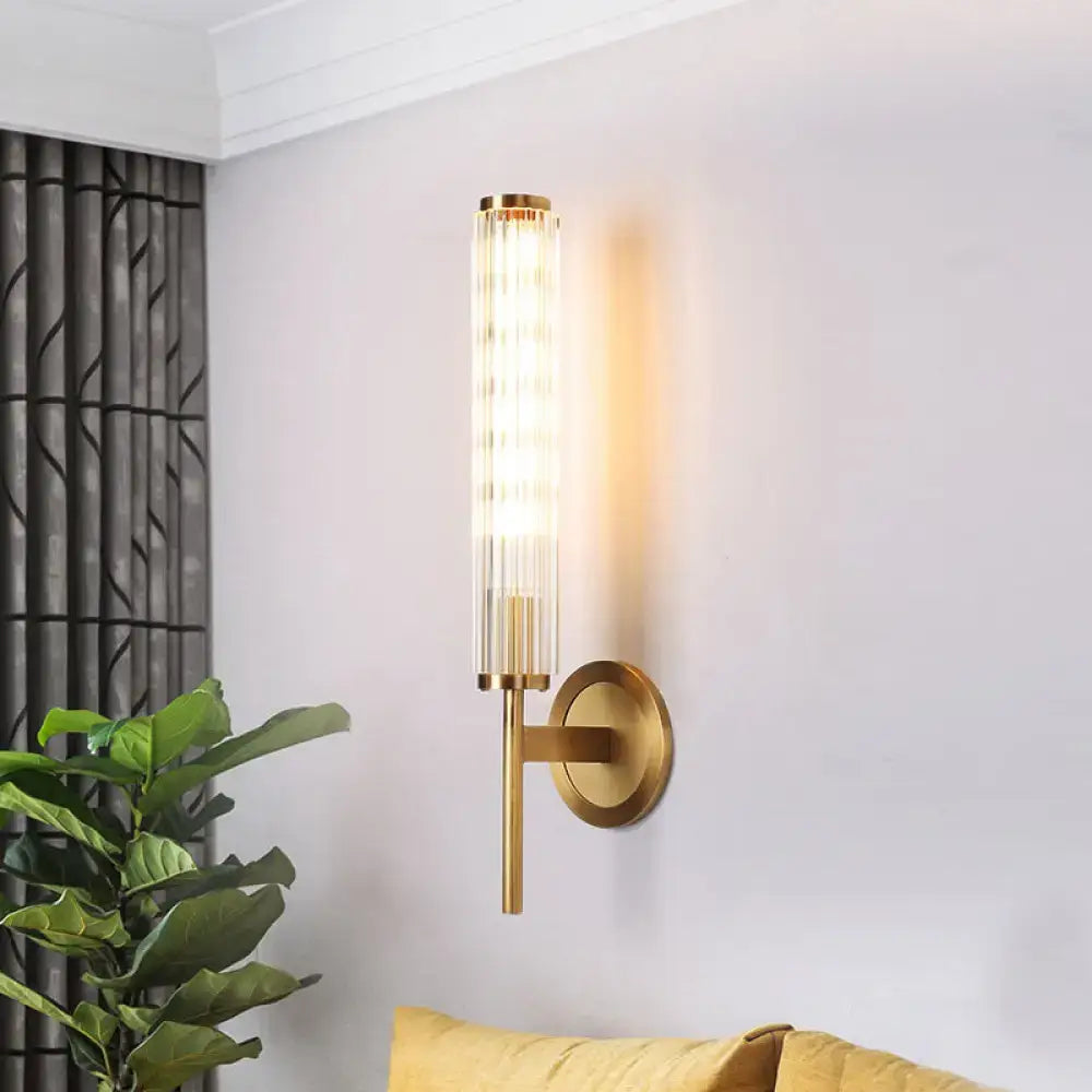 Contemporary gold brass cylinder wall light fixture with cylindrical ridged glass shade and warm diffused lighting
