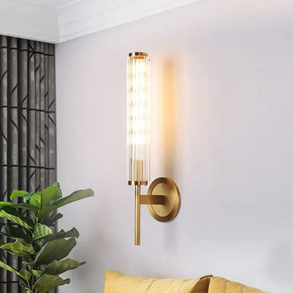 Contemporary gold brass cylinder wall light fixture with cylindrical ridged glass shade and warm diffused lighting