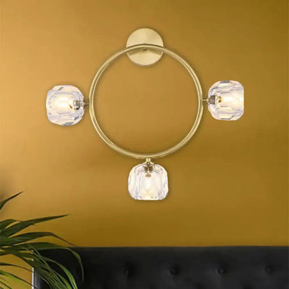 Contemporary gold brass wall light fixture with circular design and three faceted crystal shades for bedroom use