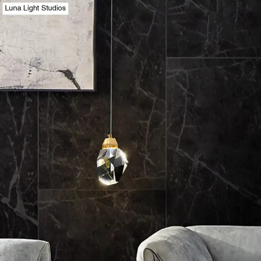 Decorbites crystal stone-shape pendant light fixture with faceted crystal and gold-toned top against dark marble wall