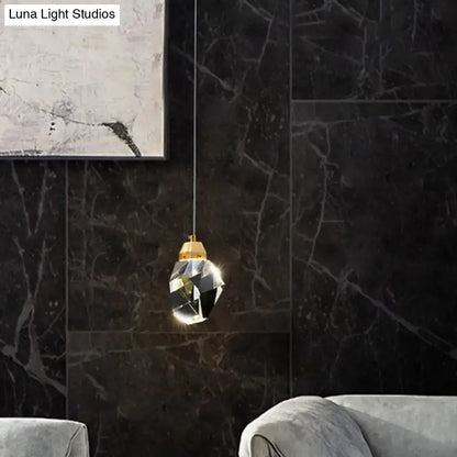 Decorbites crystal stone-shape pendant light fixture with faceted crystal and gold-toned top against dark marble wall