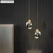 Two elegant DecorBites™ crystal stone-shape pendant light fixtures with gold tops hang against a dark ribbed wall